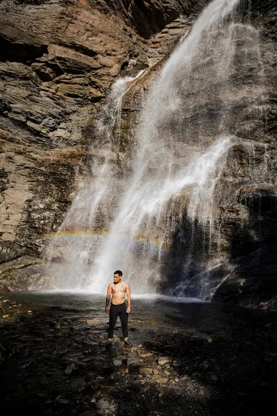 Şelale ve gökkuşağının yanında kendine güvenen bir adam