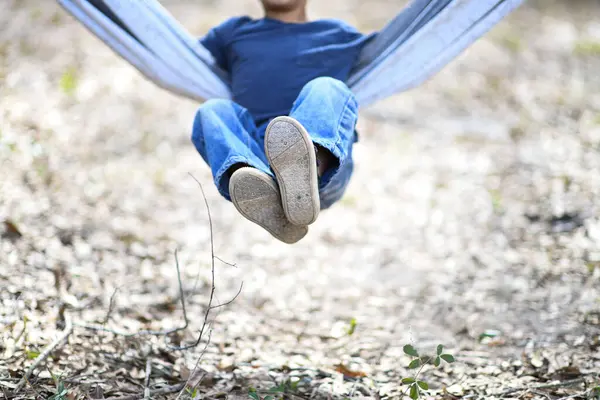 Çocuk hamakta sallanıyor, bacakları şakacı bir şekilde kalkıyor.