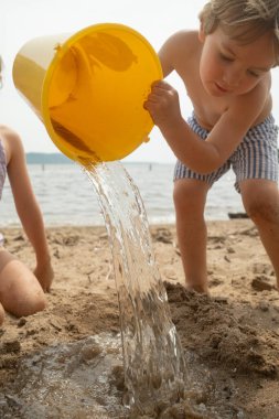 Çocuk sarı kovadan kumsala su döker..