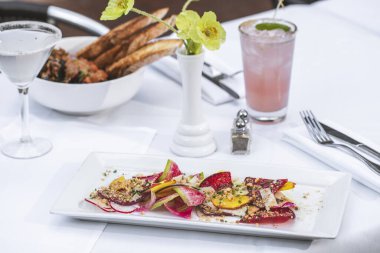 Salata ve yiyecek beyaz masada içeceklerle dolup taşıyor.