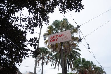 Sydney 'de palmiye ağaçlarının arasında asılı ANZAC Günü afişi