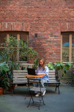 Samimi bir avluda, saksıda dizüstü bilgisayarda çalışan bir kadın.
