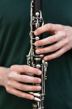 Yeşil bir gömleğe karşı klarnet çalan bir adamın ellerinin yakın çekimi.