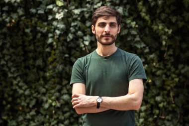 Kollarını kavuşturmuş yeşil tişört giyen bir adamın portresi.