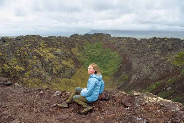 İzlanda 'da Eldborg volkanik krater kenarında oturan ceketli kadın.