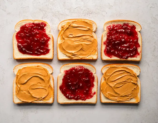 Üst manzara fıstık ezmesi ve reçel beyaz ekmek dilimlerine yayılmış..