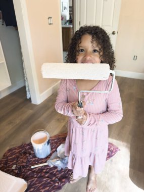 Pembe elbiseli gülümseyen kız yeni boyanmış boya silindiri tutuyor.