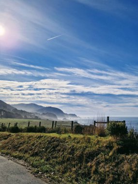 Sahil manzarası, berrak mavi gökyüzü ve yuvarlanan tepeler altında.