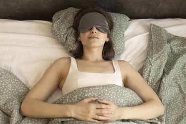 Yatakta ipek uyku maskesi takan bir kadın.