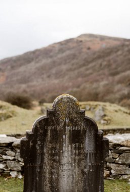 Taştan duvarlı kırsal mezarlıkta yıpranmış mezar taşı, Ulpha
