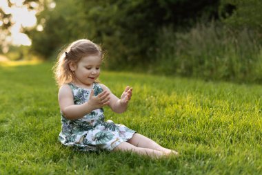 Kız çimlerin üzerinde oturuyor ve ellerine bakıyor.