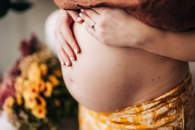 Çiçekli pantolonlu ellerin sardığı hamile göbeğinin yakın çekimi.