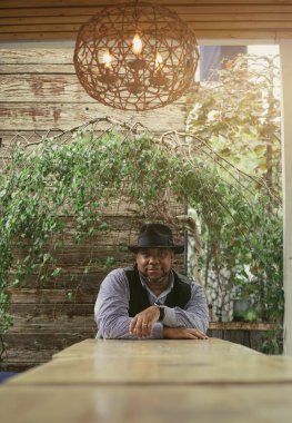 Siyahi bir adam yeşil bir zemine karşı masada oturuyor.