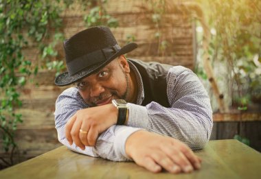 Siyahi bir adam yeşil bir zemine karşı masada oturuyor.