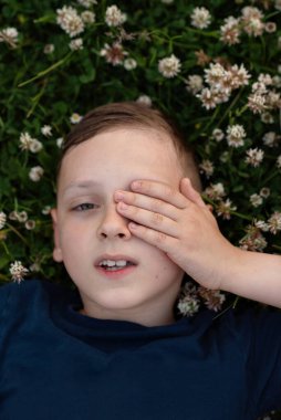 Yonca tarlasında yatan çocuk, kameraya bakıyor, tek gözünü kapatıyor..