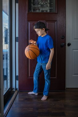 Çocuk, ahşap bir ön kapının yanında basketbol oynuyor.
