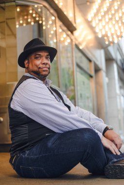 Zenci bir adam bir sinemanın parlayan ışıklarının önünde oturur.