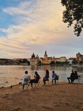 İnsanlar gün batımında Prag 'da nehir kenarında dinleniyorlar.