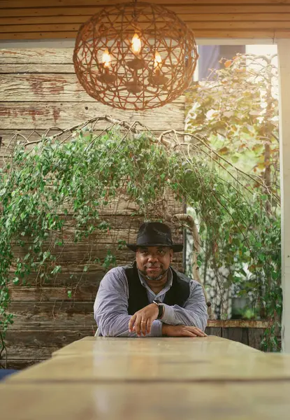 Siyahi bir adam yeşil bir zemine karşı masada oturuyor.