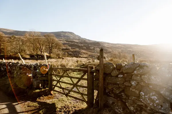 Tahta kapı ve taştan duvar. Uzakta güneşli tepeler var..
