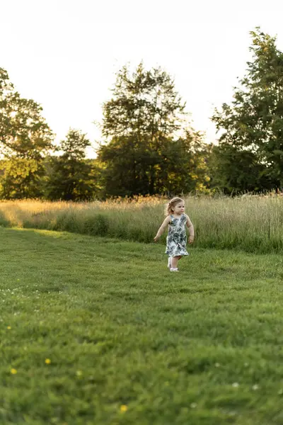 Kız gün batımında çimlerin arasında parkta yürüyor.