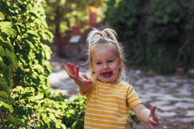 Küçük kız dışarıda oynuyor ve büyük bir gülümsemeyle doğanın tadını çıkarıyor.