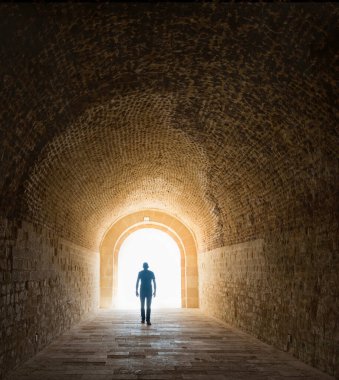 Karanlıktan aydınlığa yürüyen bir adamın silüeti.