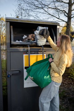 Dışarıdaki çöp kutusuna kullanılmış giysiler bağışlayan bir kadın.
