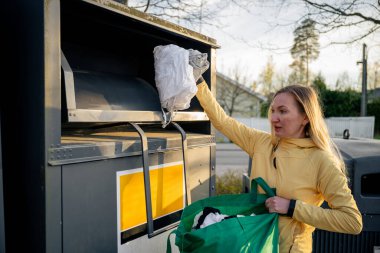 Eski giysileri geri dönüşüm kutularına koyan kadın.