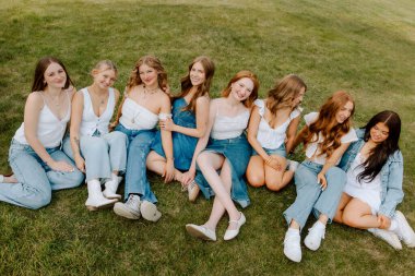 Üniversite öğrencileri kot ve beyaz kıyafetler giyip çimlerin üzerinde dinleniyorlar.