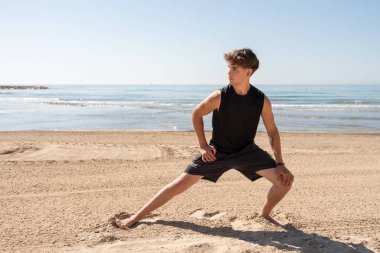 Genç bir adam antrenman sırasında kumsalda geriniyor.