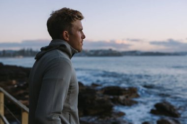 Sporcu eğitimden sonra gün batımında okyanusa bakıyor.