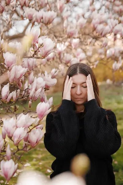 Manolya ağacının yanında baş ağrısı çeken genç bir kadın.