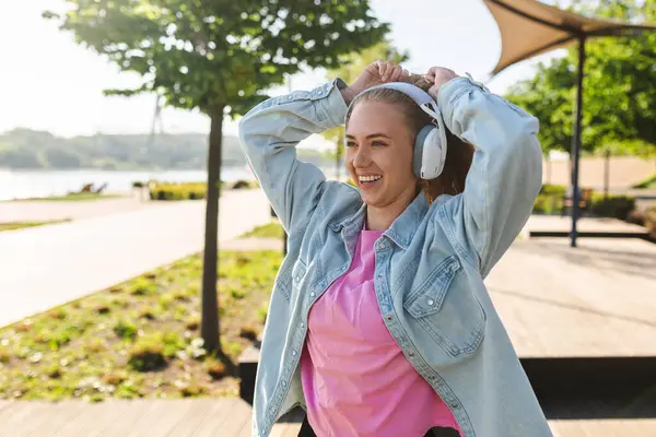 Kulaklıklı gülümseyen kadın açık havada müzik dinliyor.