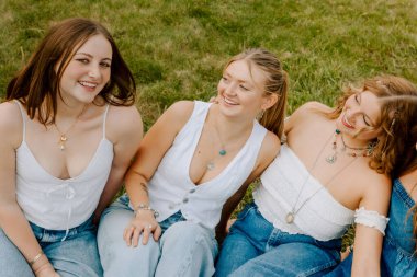 Üniversite öğrencileri beyaz bluz ve çimlerin üzerinde kot pantolon giyiyor.