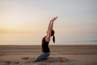 Gün doğumunda sahilde yoga yapan bir kadın.
