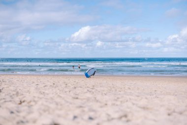 Arka planda sörfçülerle kumlu sahilde duran bir vücut tahtası.