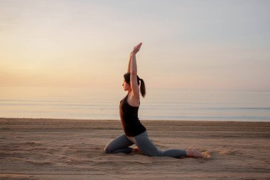 Gün doğumunda sahilde yoga yapan bir kadın.
