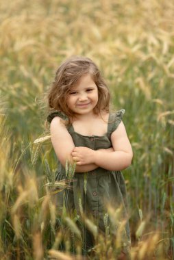 Mutlu, gülümseyen küçük kız buğday tarlasında duruyor.