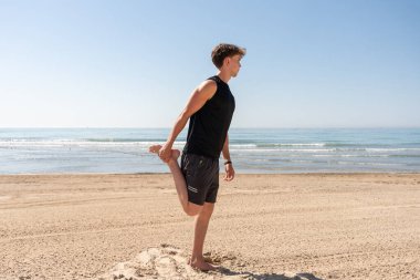 Genç bir adam antrenman sırasında kumsalda geriniyor.