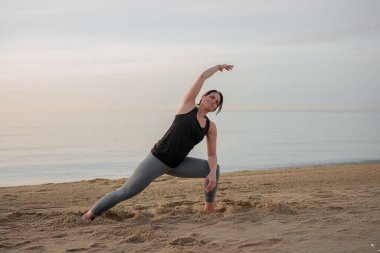 Gün doğumunda sahilde yoga yapan bir kadın.