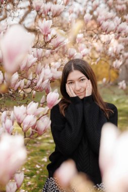 Genç bir kadın yüzüne dokunuyor, baharda çiçek açan manolyalar.