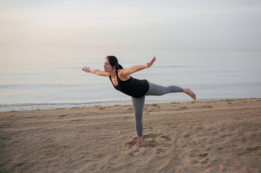 Gün doğumunda sahilde yoga yapan bir kadın.