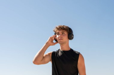 Kulaklıklı genç sporcu sahilde gökyüzünü izliyor.