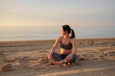 Gün doğumunda sahilde yoga yapan bir kadın.