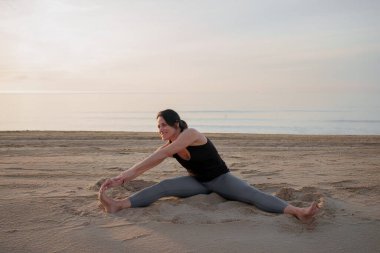 Gün doğumunda sahilde yoga yapan bir kadın.