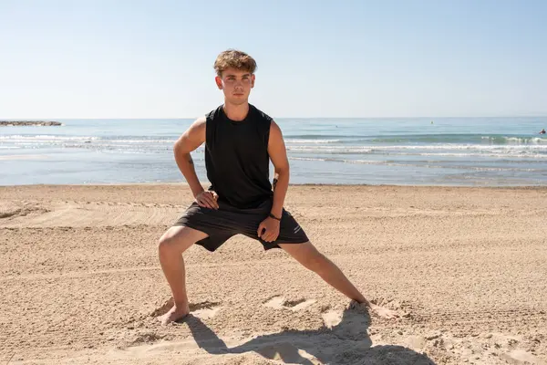 Genç bir adam antrenman sırasında kumsalda geriniyor.