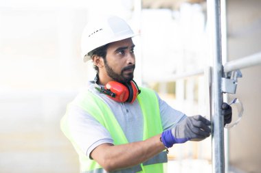 Beyaz miğferi ve güvenlik yeleği olan işçi ahşap bir ev inşa ediyor.