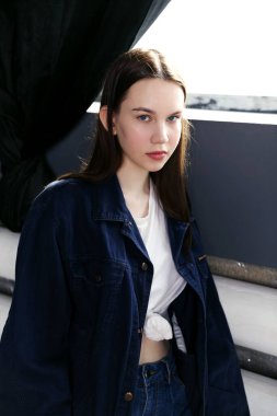 Penceresi ve siyah arka planı olan genç bir kadın model oturuyor.