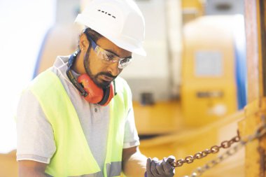 Beyaz miğferi ve güvenlik yeleği olan işçi ahşap bir ev inşa ediyor.